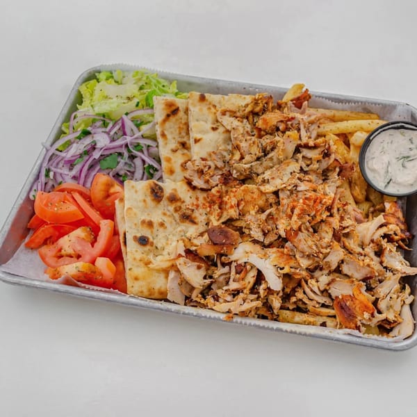 A Greek chicken gyro platter with pita bread, fries, salad, tomatoes, and tzatziki sauce.