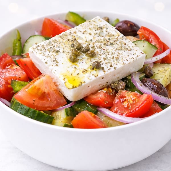 A close-up of a Greek salad with a large block of feta cheese, tomatoes, cucumbers, and olives.