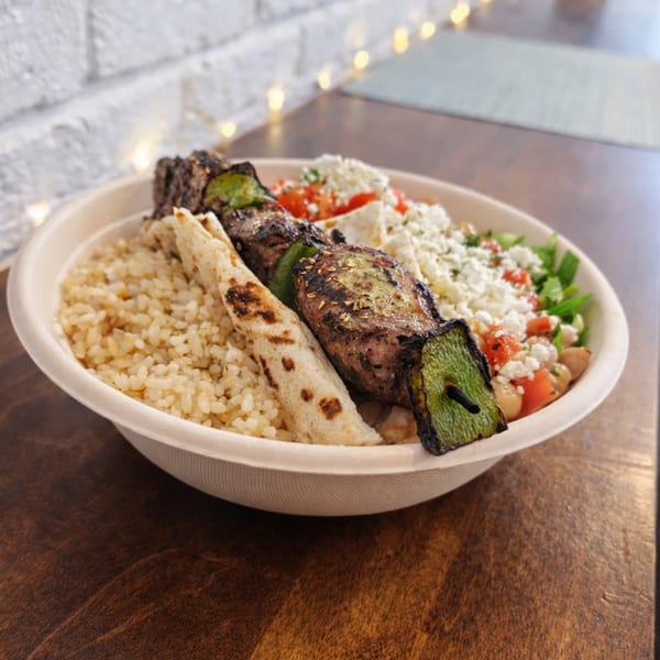 Greek souvlaki bowl with grilled meat and peppers, rice, pita, feta, and tomatoes.