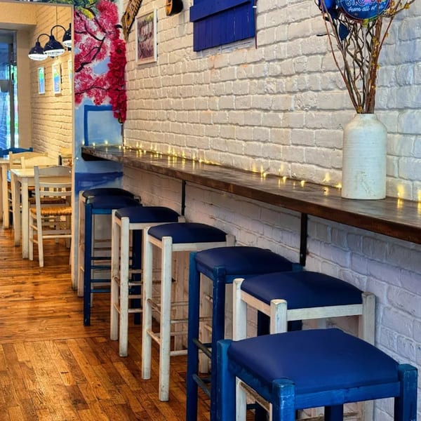 A row of blue and white bar stools along a counter with string lights in a Greek restaurant.