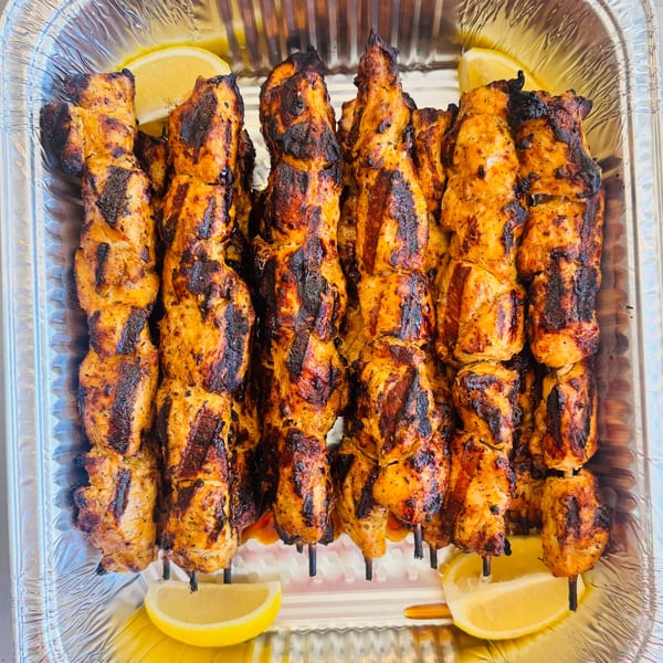 Grilled chicken souvlaki skewers with charred marks and lemon wedges in a foil tray.